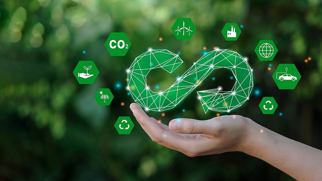 Mão de pessoa segurando um desenho representando um ciclo infinito, cercado por ícones menores que representam tecnologias verdes